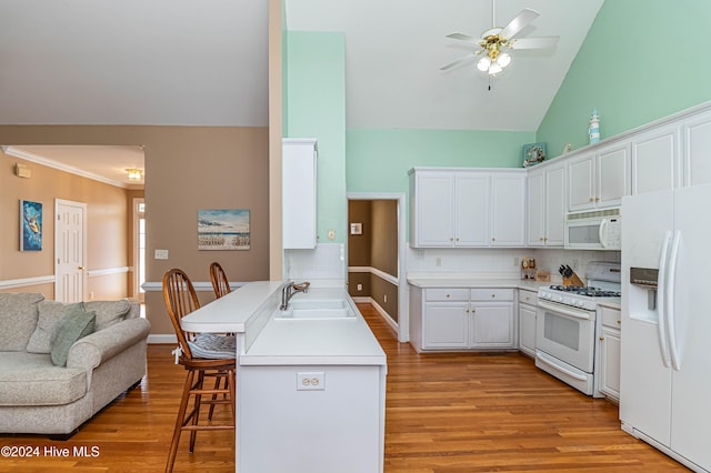 kitchen with sink, backsplash, white appliances, a breakfast bar area, and white cabinets