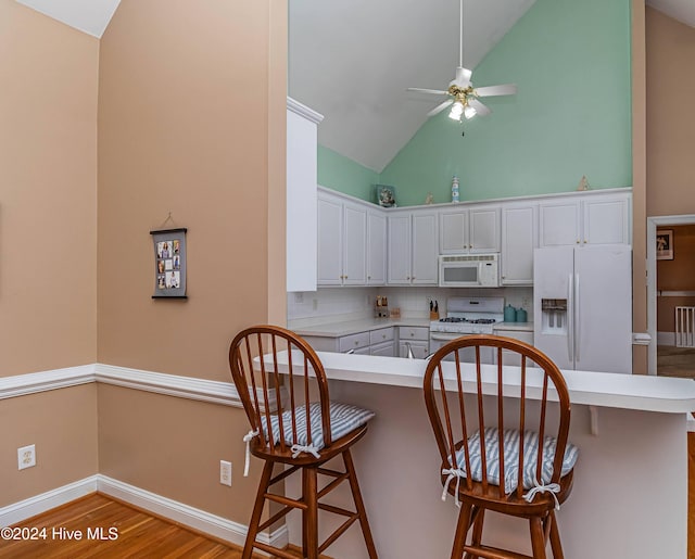 kitchen featuring white cabinetry, white appliances, a breakfast bar area, and tasteful backsplash