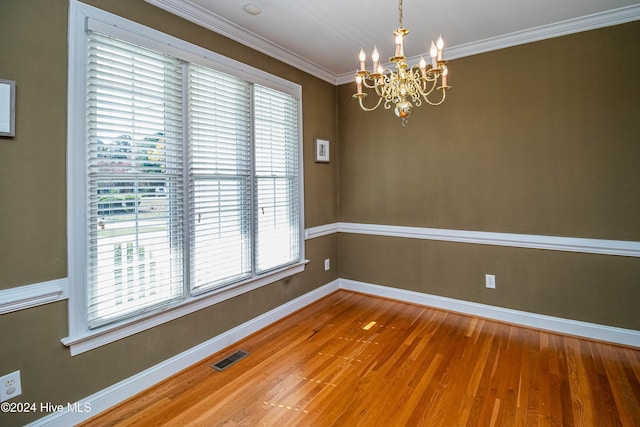 spare room with a chandelier, crown molding, a healthy amount of sunlight, and wood-type flooring