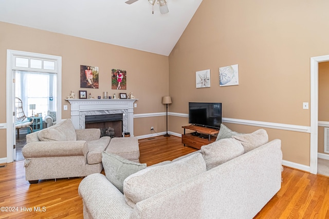 living room featuring a high end fireplace, light hardwood / wood-style flooring, high vaulted ceiling, and ceiling fan