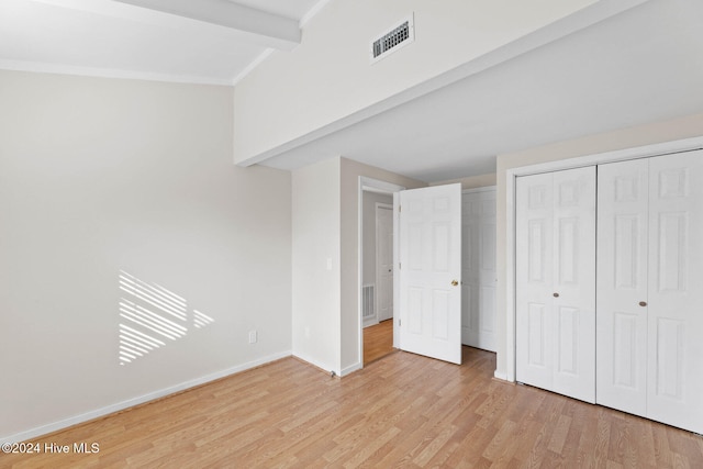 unfurnished bedroom with beamed ceiling, light hardwood / wood-style floors, and a closet