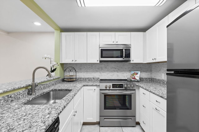 kitchen with light stone countertops, backsplash, stainless steel appliances, sink, and white cabinetry