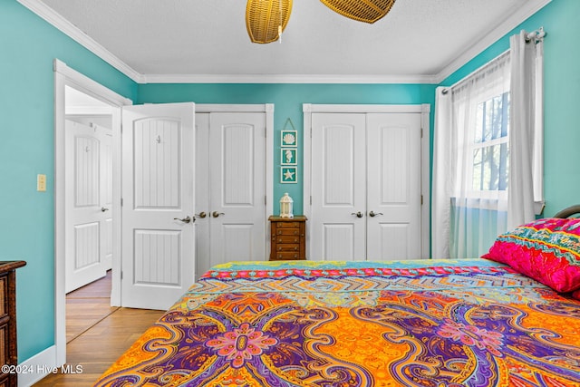 bedroom featuring a textured ceiling, hardwood / wood-style flooring, ceiling fan, crown molding, and multiple closets