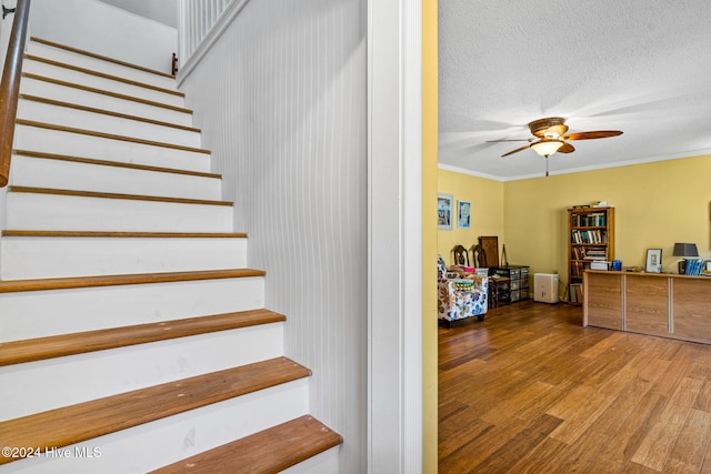 staircase featuring hardwood / wood-style floors, ceiling fan, a textured ceiling, and ornamental molding