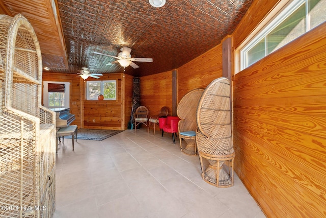 sitting room with wooden walls, tile patterned flooring, and ceiling fan