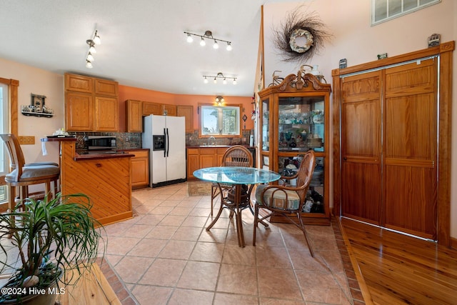 kitchen featuring sink, white fridge with ice dispenser, rail lighting, tasteful backsplash, and a kitchen breakfast bar