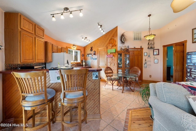 kitchen with a kitchen breakfast bar, track lighting, vaulted ceiling, white refrigerator, and hanging light fixtures