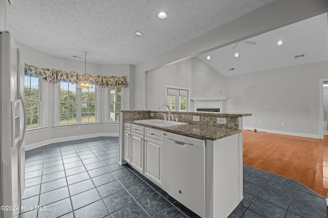 kitchen with lofted ceiling, white appliances, a kitchen island with sink, sink, and white cabinetry