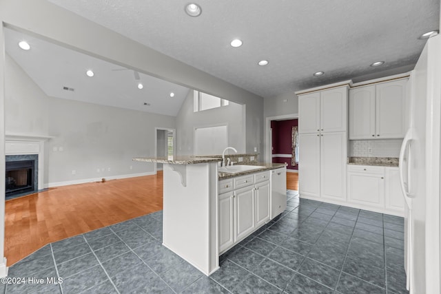 kitchen featuring sink, dark hardwood / wood-style floors, lofted ceiling, a kitchen island with sink, and white cabinets