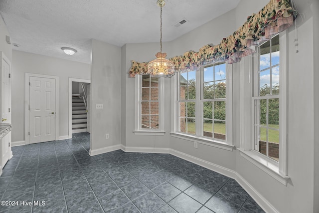 unfurnished dining area featuring plenty of natural light, dark tile patterned floors, a textured ceiling, and an inviting chandelier