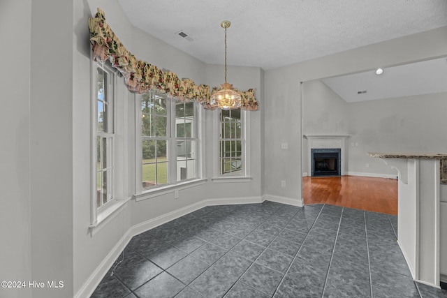 interior space with a high end fireplace, a textured ceiling, vaulted ceiling, dark tile patterned floors, and a chandelier