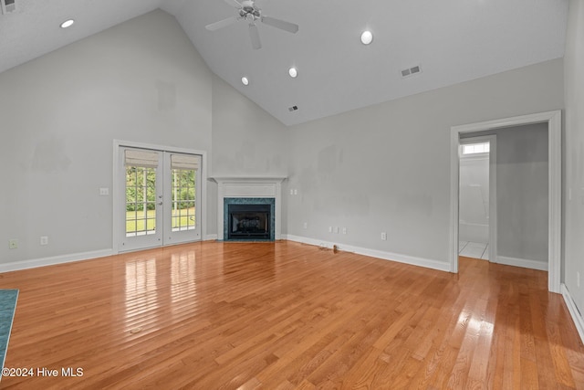 unfurnished living room with high vaulted ceiling, french doors, light hardwood / wood-style flooring, ceiling fan, and a fireplace