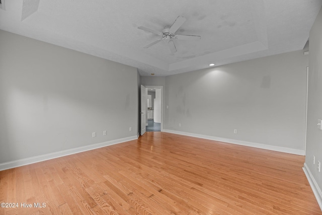 unfurnished room featuring ceiling fan, light wood-type flooring, a textured ceiling, and a tray ceiling