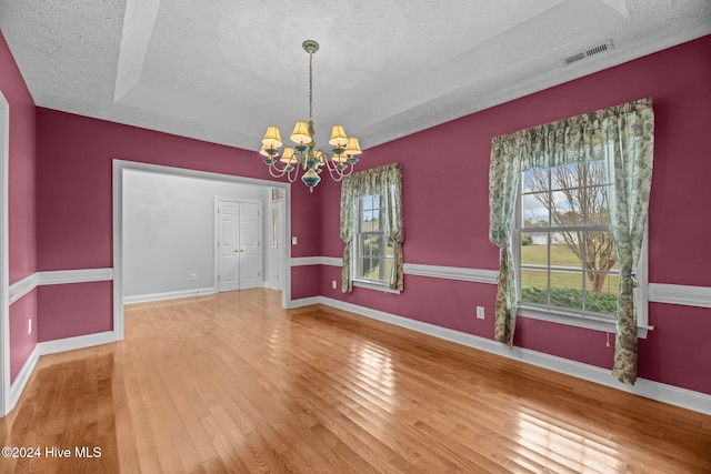 empty room with an inviting chandelier, a textured ceiling, and hardwood / wood-style flooring