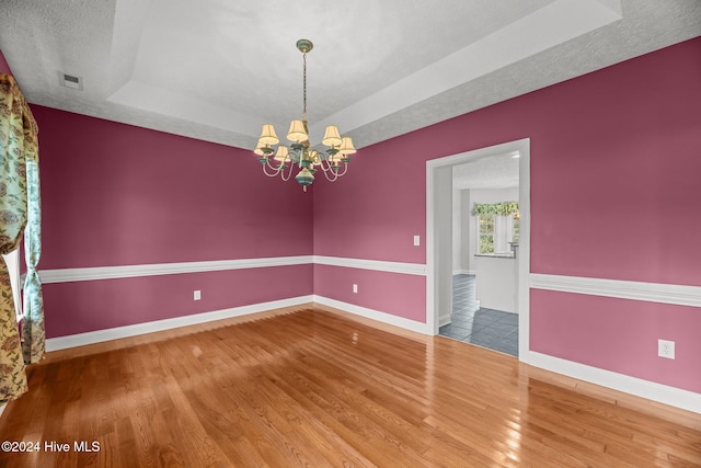 empty room featuring a tray ceiling, a chandelier, wood-type flooring, and a textured ceiling