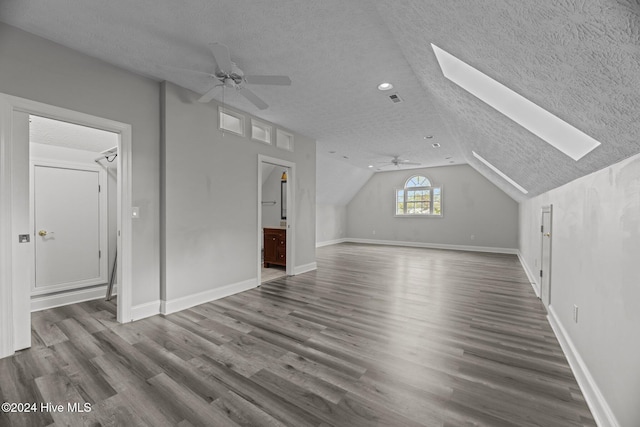 additional living space featuring hardwood / wood-style floors, a textured ceiling, ceiling fan, and vaulted ceiling with skylight