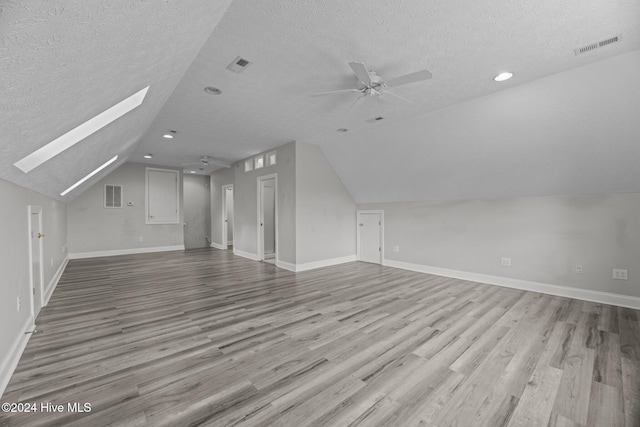 bonus room featuring a textured ceiling, light hardwood / wood-style flooring, ceiling fan, and vaulted ceiling with skylight