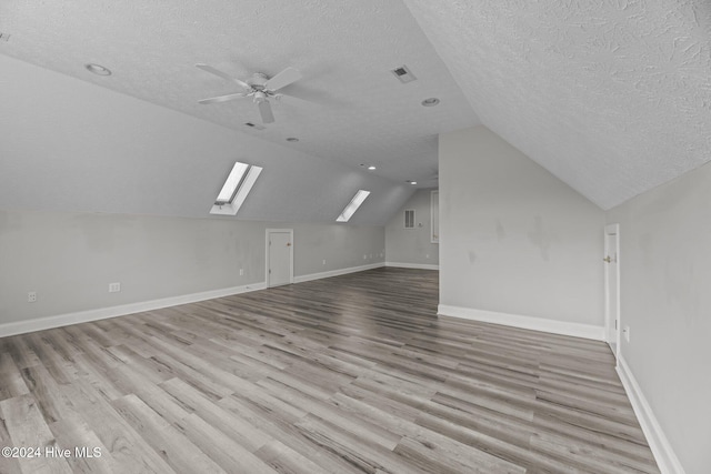 bonus room featuring lofted ceiling with skylight, ceiling fan, light hardwood / wood-style floors, and a textured ceiling