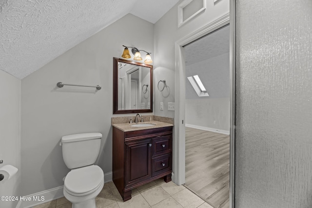 bathroom with wood-type flooring, a textured ceiling, toilet, vaulted ceiling with skylight, and vanity