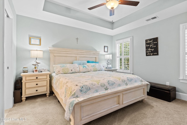 carpeted bedroom featuring a tray ceiling and ceiling fan