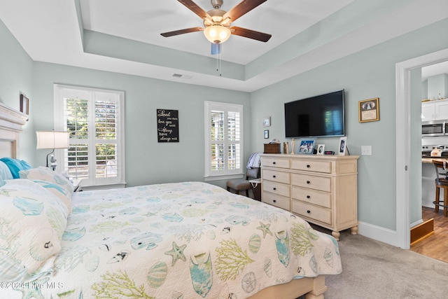 bedroom featuring light hardwood / wood-style floors, a tray ceiling, multiple windows, and ceiling fan