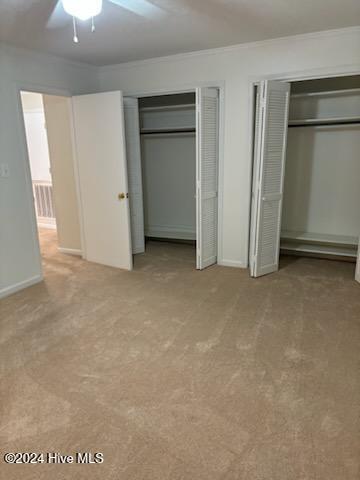 unfurnished bedroom featuring light colored carpet, ceiling fan, crown molding, and two closets