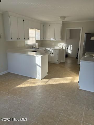 kitchen with kitchen peninsula, light tile patterned floors, crown molding, white cabinetry, and stainless steel fridge