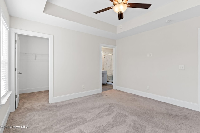 unfurnished bedroom with light carpet, ceiling fan, a raised ceiling, a closet, and a walk in closet