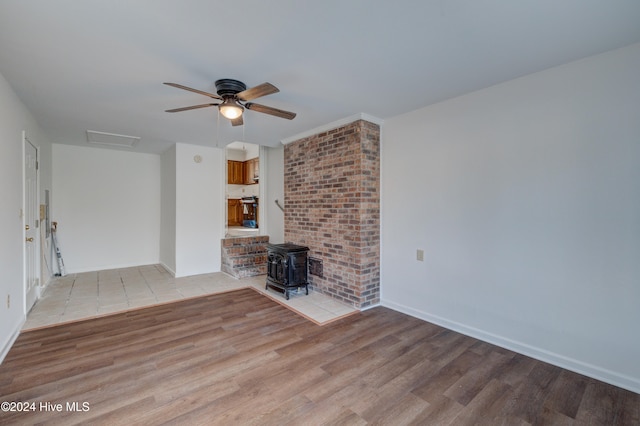 unfurnished living room with ceiling fan, a wood stove, and light hardwood / wood-style flooring