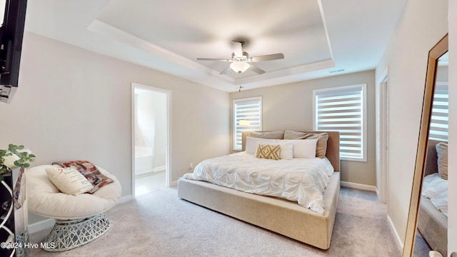 carpeted bedroom with a tray ceiling, ceiling fan, and ensuite bathroom