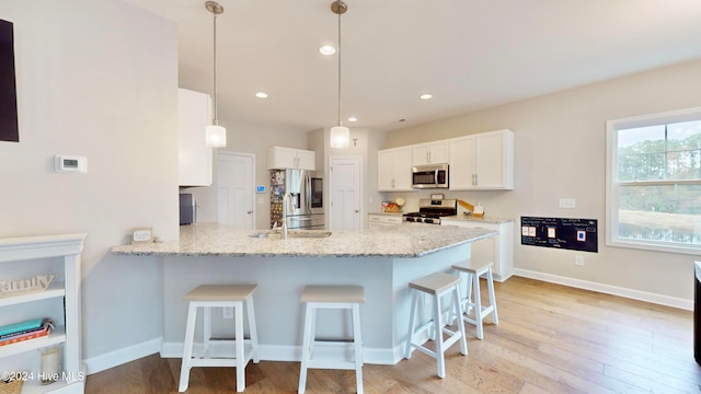 kitchen with kitchen peninsula, appliances with stainless steel finishes, a kitchen bar, white cabinets, and hanging light fixtures