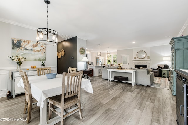 dining room with light hardwood / wood-style flooring, a chandelier, ornamental molding, and a fireplace