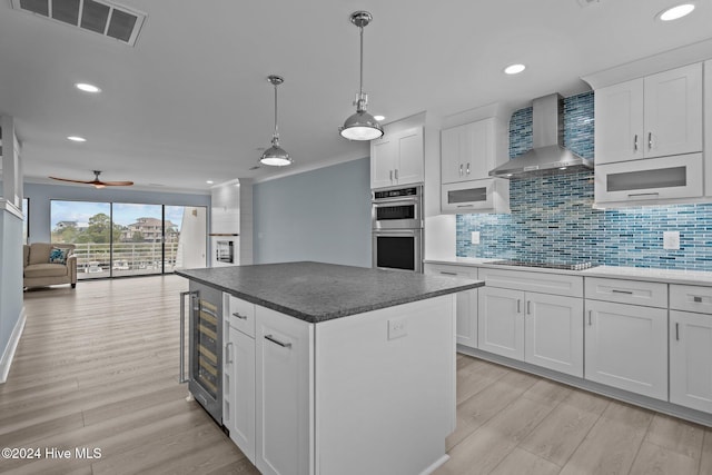 kitchen with wall chimney exhaust hood, visible vents, light wood-style flooring, and stainless steel double oven