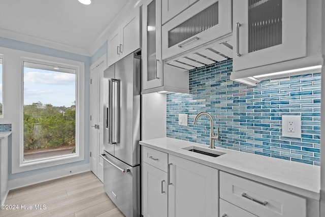 kitchen featuring high quality fridge, a sink, light countertops, white cabinetry, and backsplash