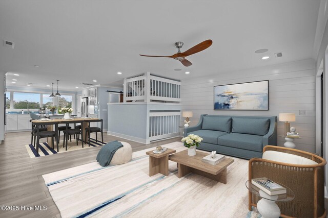 living room with crown molding, ceiling fan, wooden walls, and light hardwood / wood-style floors