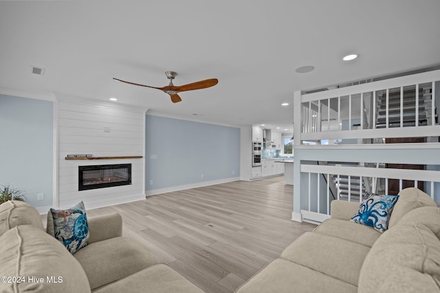 living room with ornamental molding, light hardwood / wood-style floors, a large fireplace, and ceiling fan