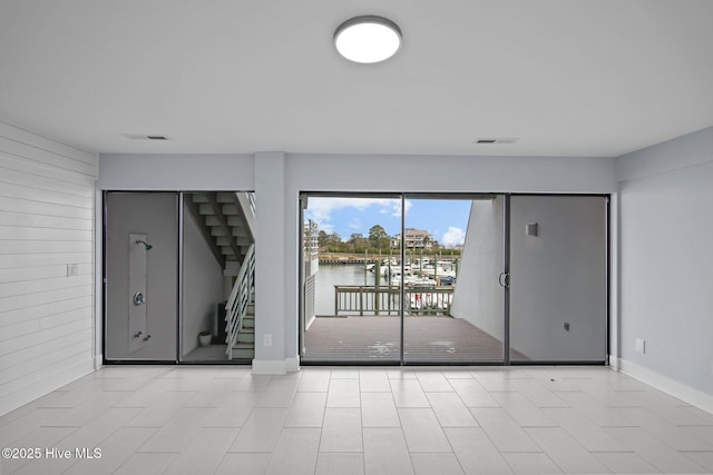 spare room featuring wooden walls, a water view, visible vents, baseboards, and stairs