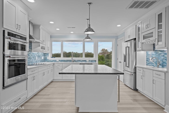 kitchen with visible vents, wall chimney exhaust hood, a kitchen island, stainless steel appliances, and a sink