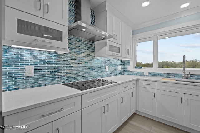 kitchen featuring wall chimney range hood, decorative backsplash, and white cabinets