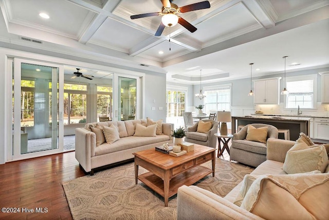 living room featuring ceiling fan with notable chandelier, light hardwood / wood-style floors, crown molding, and coffered ceiling