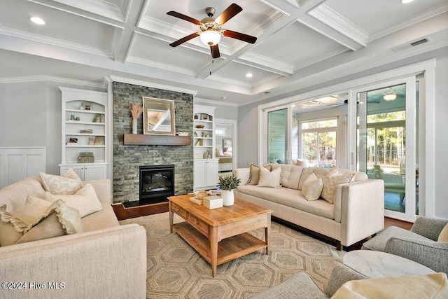 living room with beam ceiling, ceiling fan, coffered ceiling, a stone fireplace, and crown molding