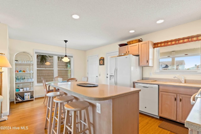 kitchen featuring light brown cabinets, hanging light fixtures, light hardwood / wood-style floors, white appliances, and a center island