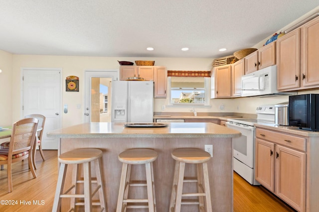 kitchen with light hardwood / wood-style floors, a breakfast bar area, white appliances, and a kitchen island