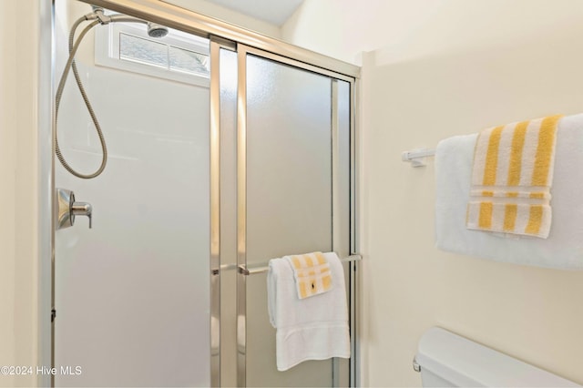 bathroom featuring a shower with door and toilet