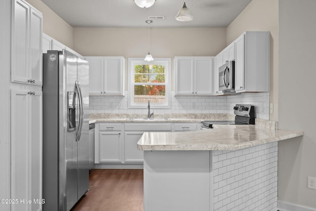 kitchen featuring hanging light fixtures, sink, kitchen peninsula, appliances with stainless steel finishes, and white cabinetry