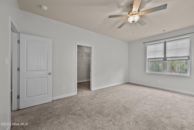 unfurnished bedroom with a walk in closet, ceiling fan, a closet, and light carpet