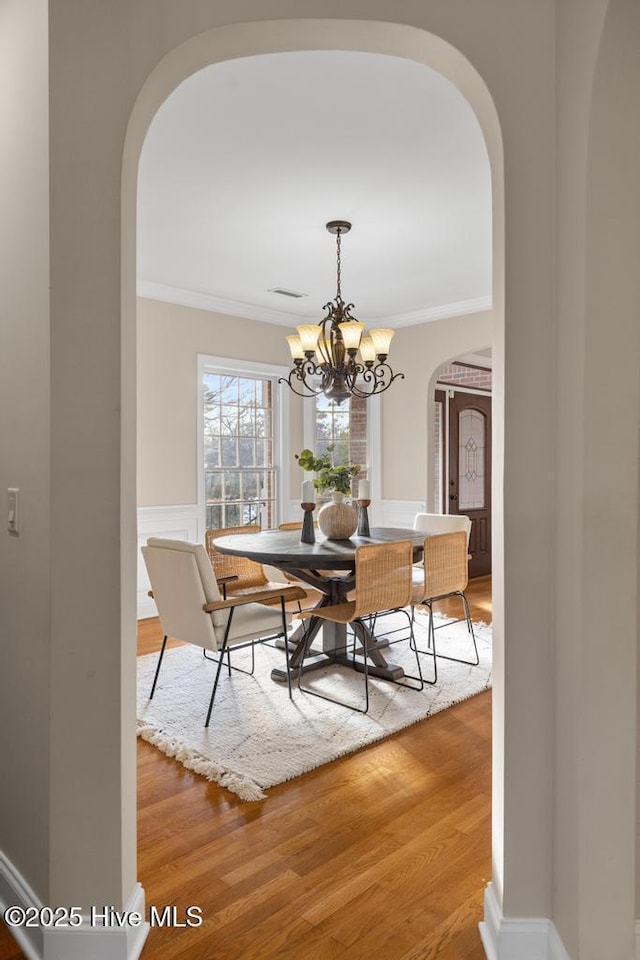 dining space with crown molding, arched walkways, a chandelier, and wood finished floors