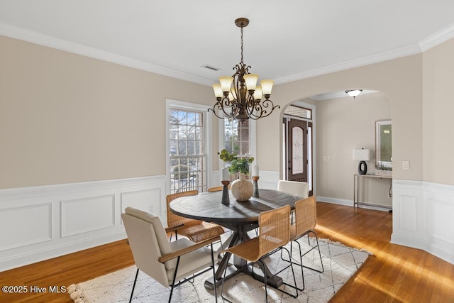 dining room with crown molding, light wood-style floors, arched walkways, visible vents, and a chandelier