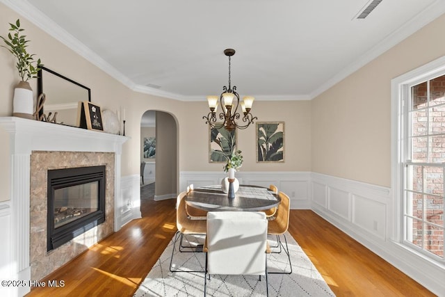 dining space with a tiled fireplace, ornamental molding, an inviting chandelier, and light hardwood / wood-style flooring