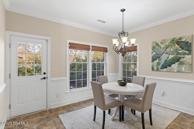 dining space with an inviting chandelier, ornamental molding, stone finish floor, wainscoting, and visible vents